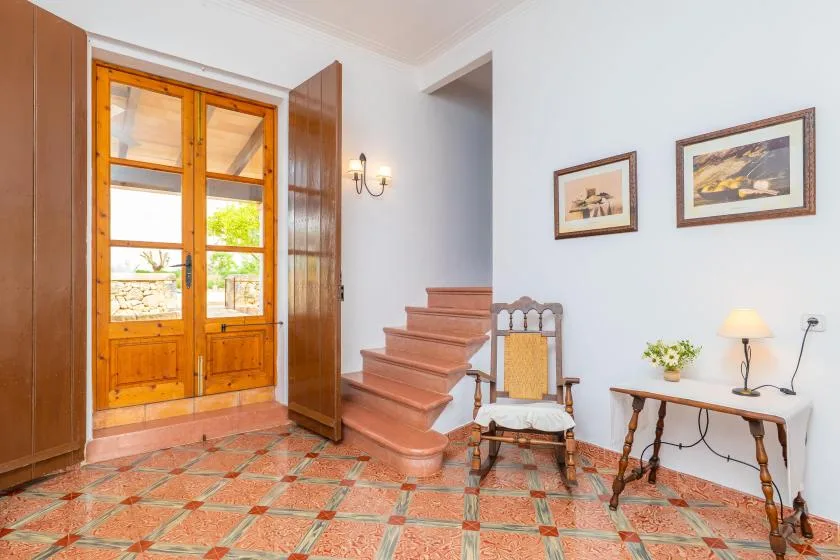 Una habitación luminosa con suelo de baldosas, puertas de madera, una escalera corta y cuadros.