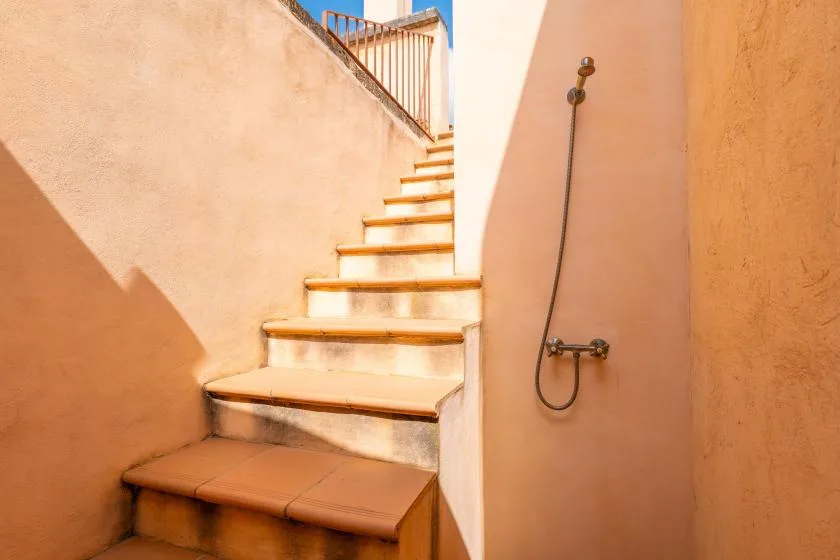 Una ducha exterior está junto a una escalera con peldaños de color terracota.