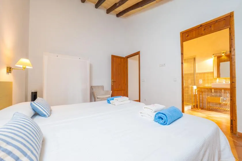 Un dormitorio con ropa de cama blanca y una puerta abierta a una habitación iluminada.