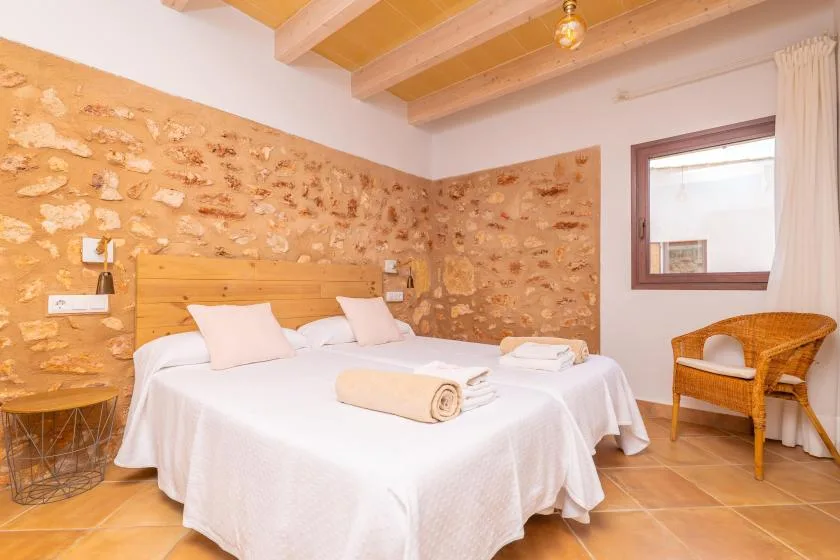 Un dormitorio con una cama blanca, paredes de piedra y una silla de mimbre.