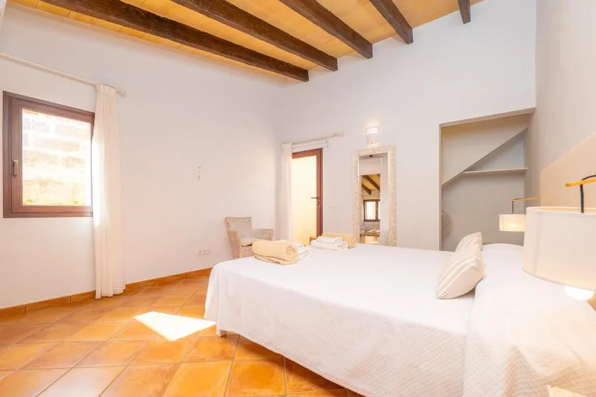 Un dormitorio luminoso con una cama grande, una ventana y vigas de madera a la vista.