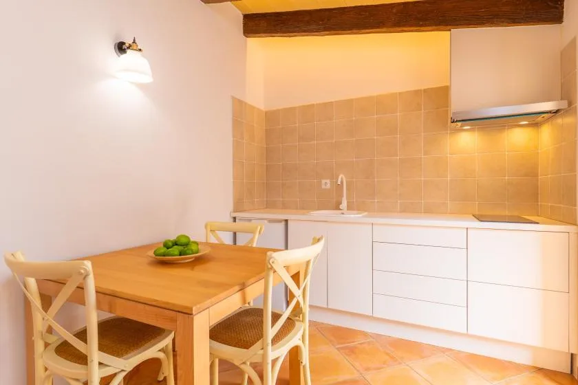 Una zona de cocina y comedor con una mesa de madera junto a armarios blancos y un salpicadero de azulejos.