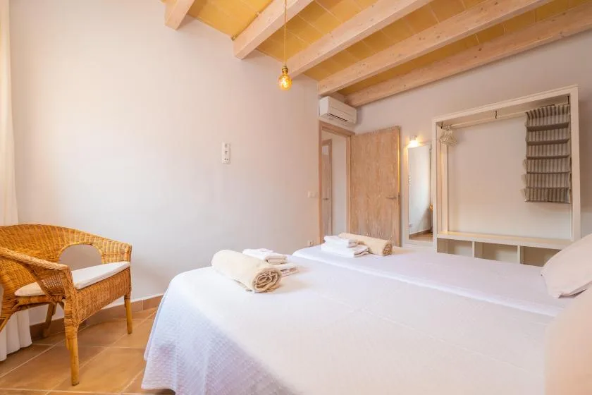 Un dormitorio con ropa de cama blanca y una silla de mimbre bajo vigas de madera vistas.