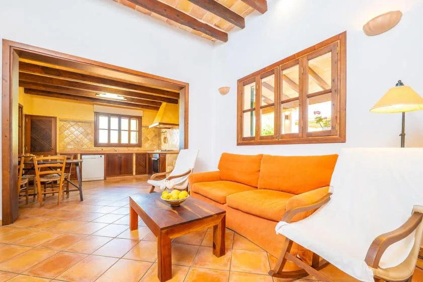 Una sala de estar con asientos naranjas, una mesa de centro de madera y una cocina abierta.