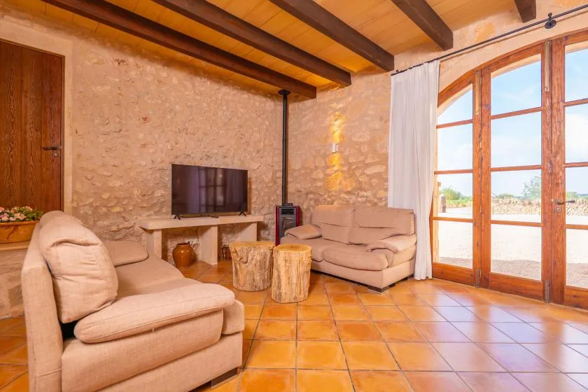 Una sala de estar con paredes de piedra, asientos claros y grandes puertas de vidrio.
