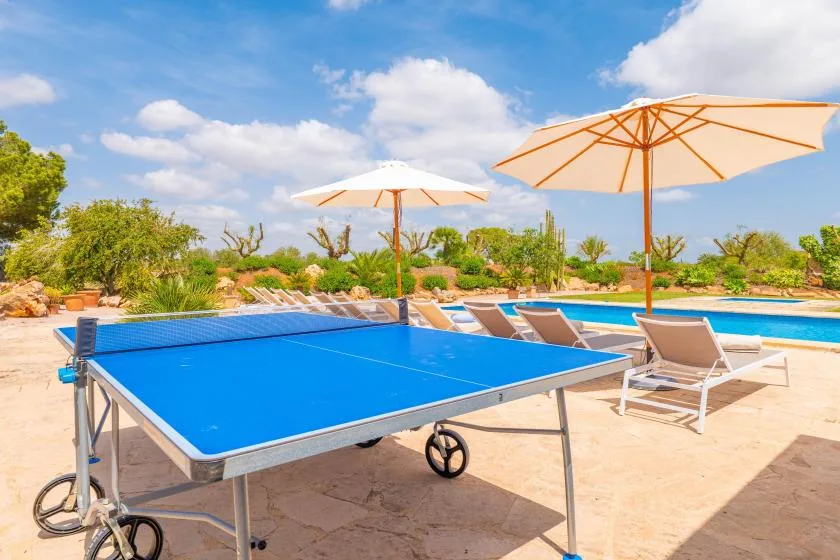 Una mesa de ping-pong al aire libre está junto a una piscina y tumbonas.