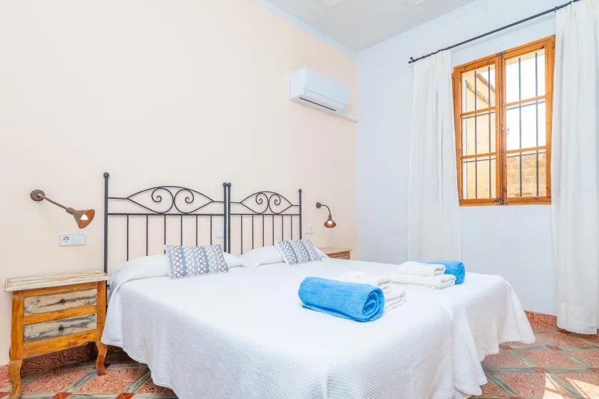 Un dormitorio luminoso con una cama doble vestida de blanco y una ventana con cortinas.