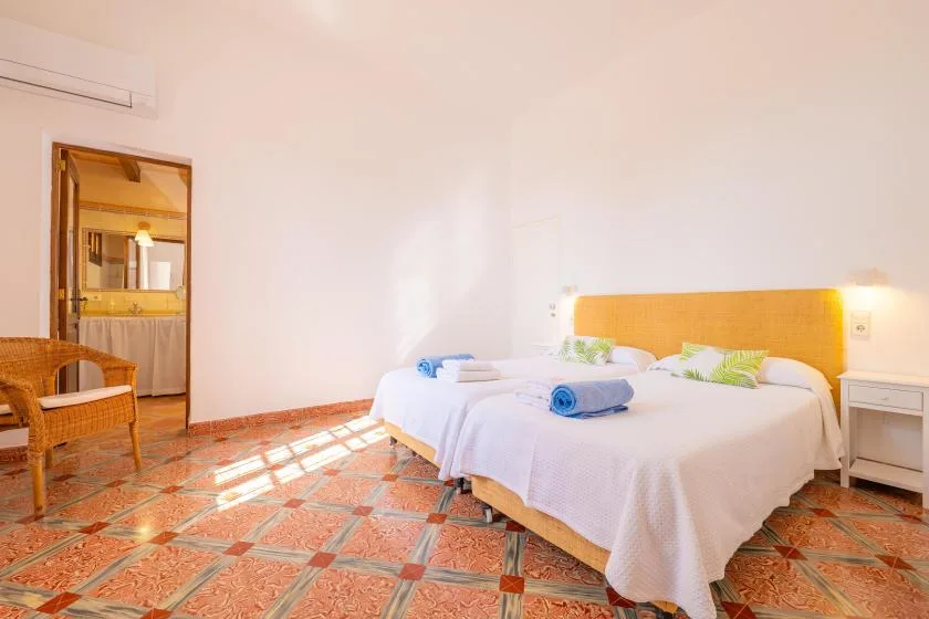 Un dormitorio luminoso con dos camas y una silla de madera.