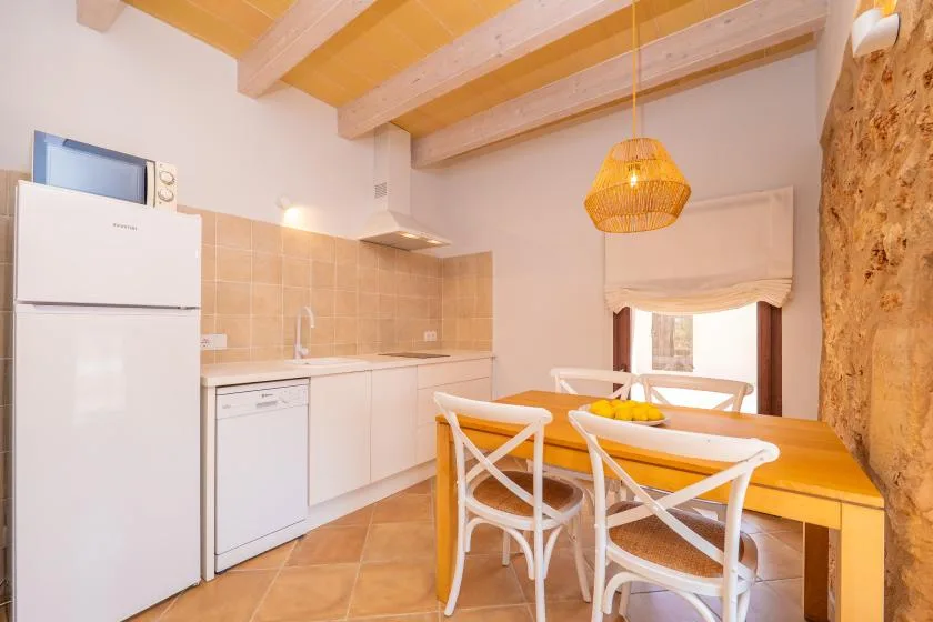Una luminosa cocina y comedor con una mesa de madera y asientos blancos.