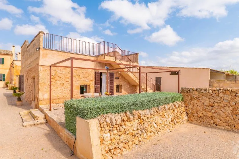 Un edificio de piedra con una escalera exterior se encuentra junto a un muro bajo de piedra.