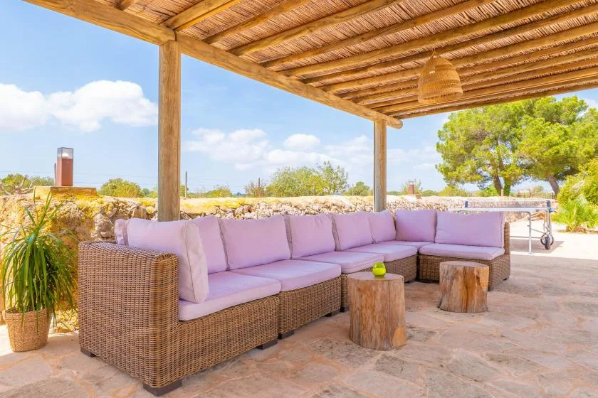 Una zona de estar al aire libre con muebles de mimbre acolchados bajo una pérgola de madera.