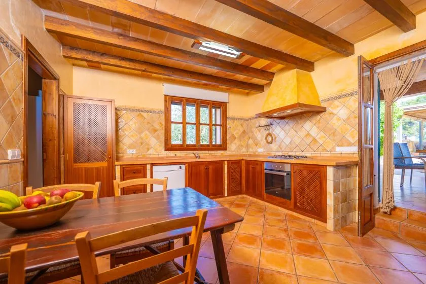 Una cocina de tonos cálidos con armarios de madera, una mesa de comedor y una puerta abierta.