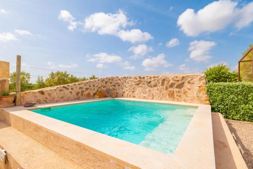 Una piscina al aire libre está junto a un muro bajo de piedra.