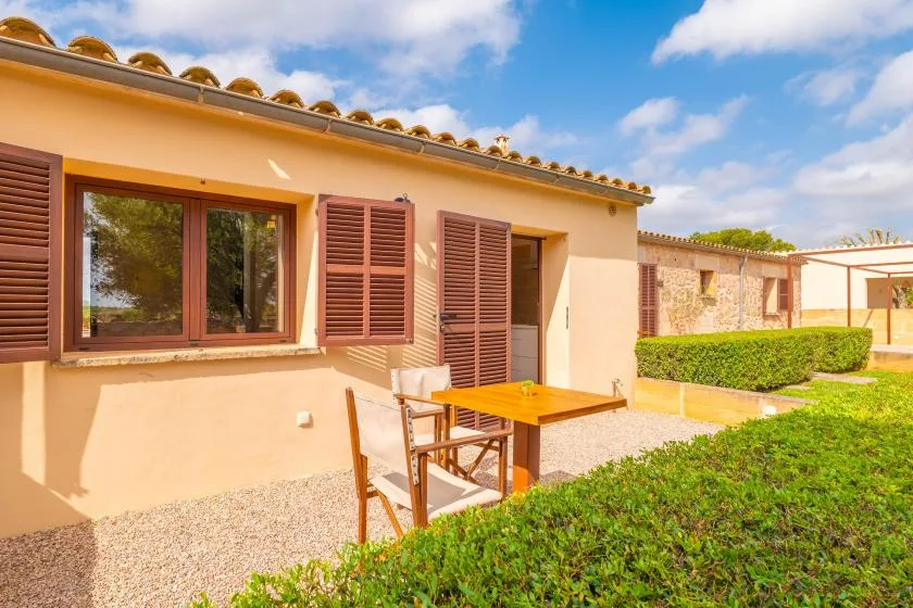 Un patio soleado con una mesa y sillas de madera junto a una casa.