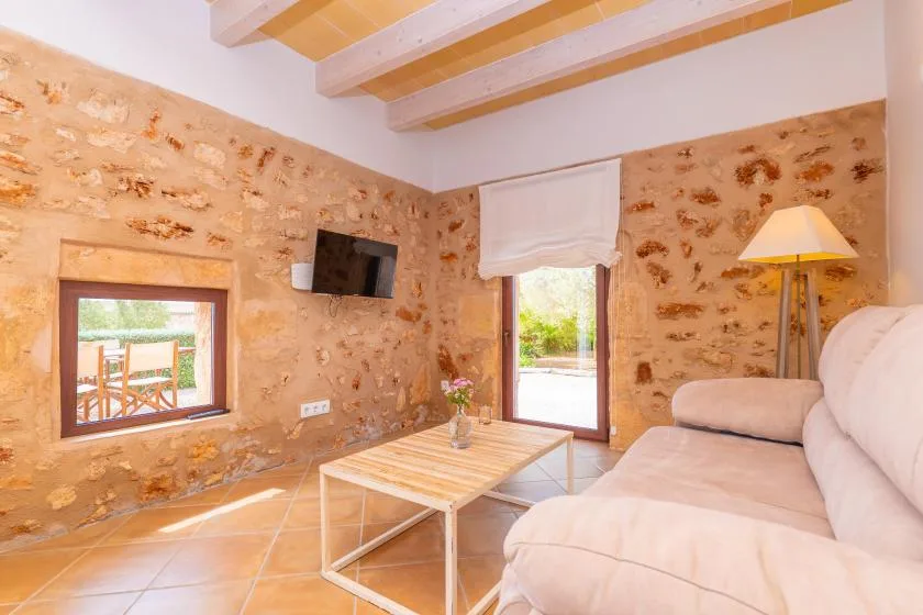 Una sala luminosa con paredes de piedra, zona de estar y vigas de madera en el techo.