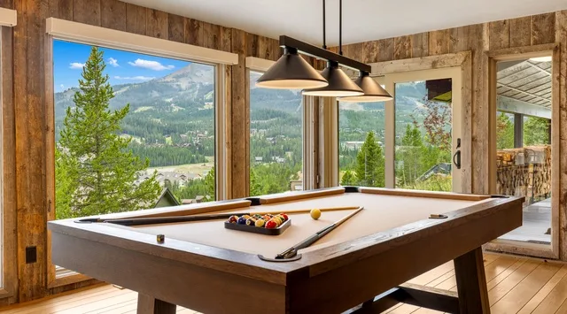 Una mesa de billar está junto a grandes ventanas con vistas a un paisaje montañoso.