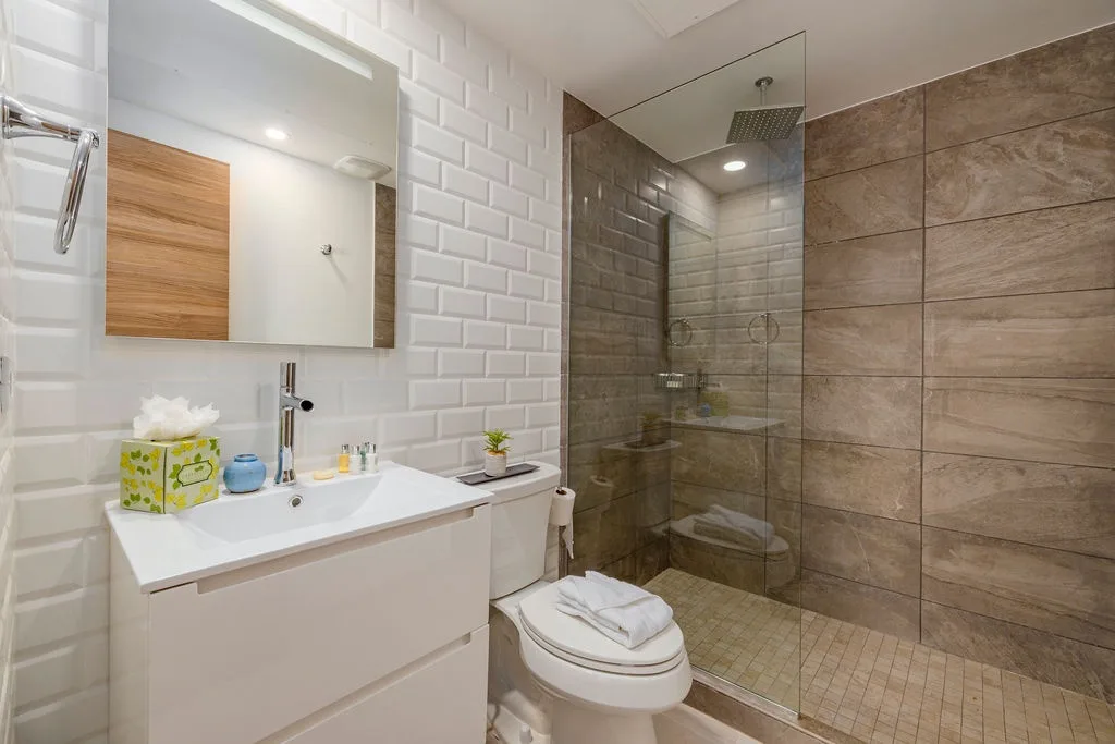Your private bathroom features white subway tiles, warm wood tones, and a sleek glass-enclosed walk-in shower