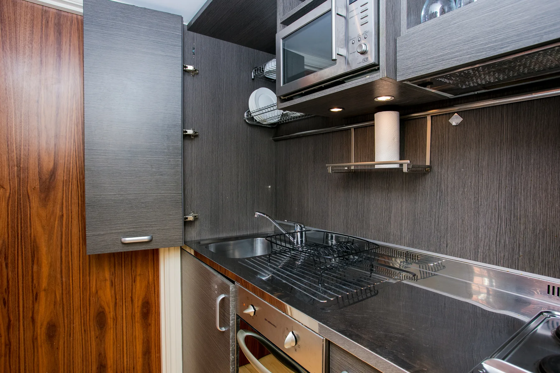 A compact kitchen with a countertop dish rack beneath overhead cabinets.