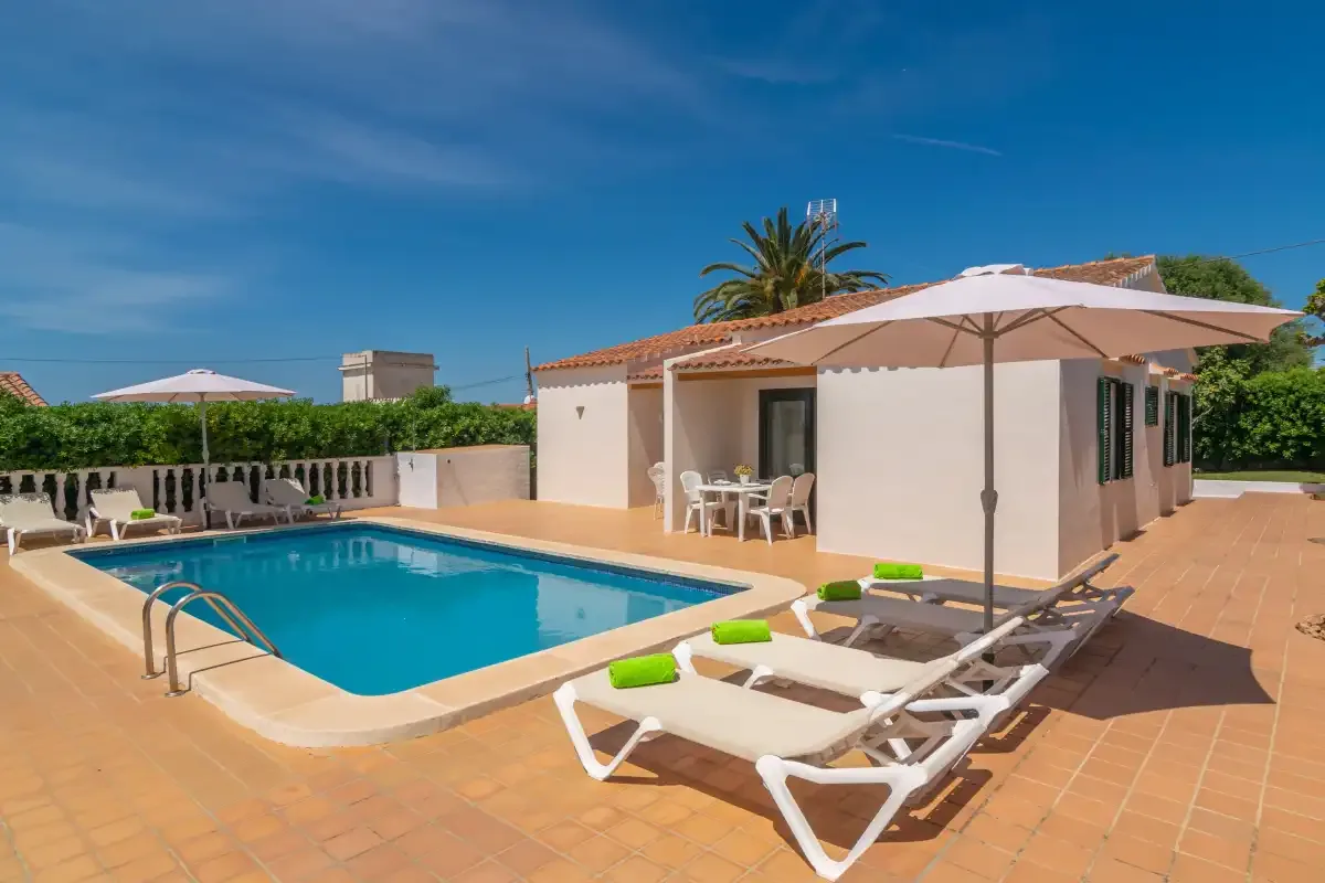 A swimming pool beside a patio with sun loungers and an umbrella.