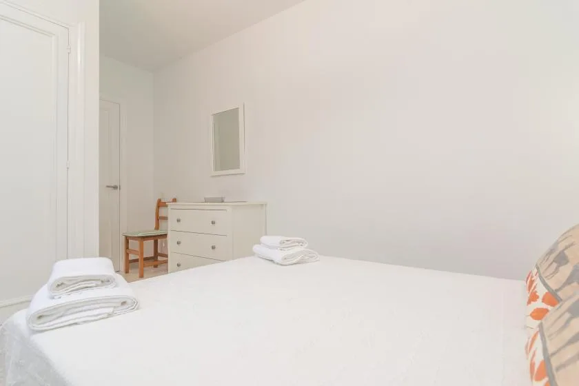 A bright bedroom with a white bed and a dresser against the wall.