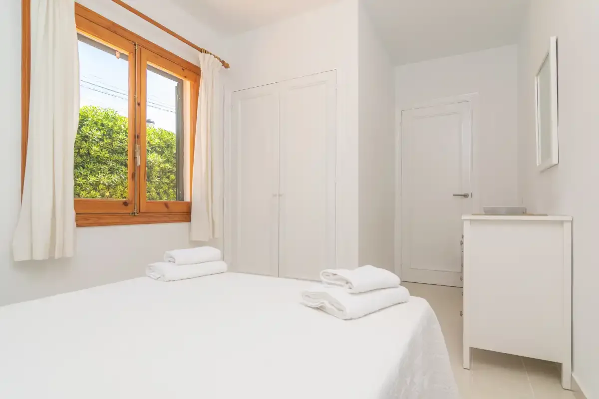A bright bedroom with a neatly made bed and a wood-framed window.