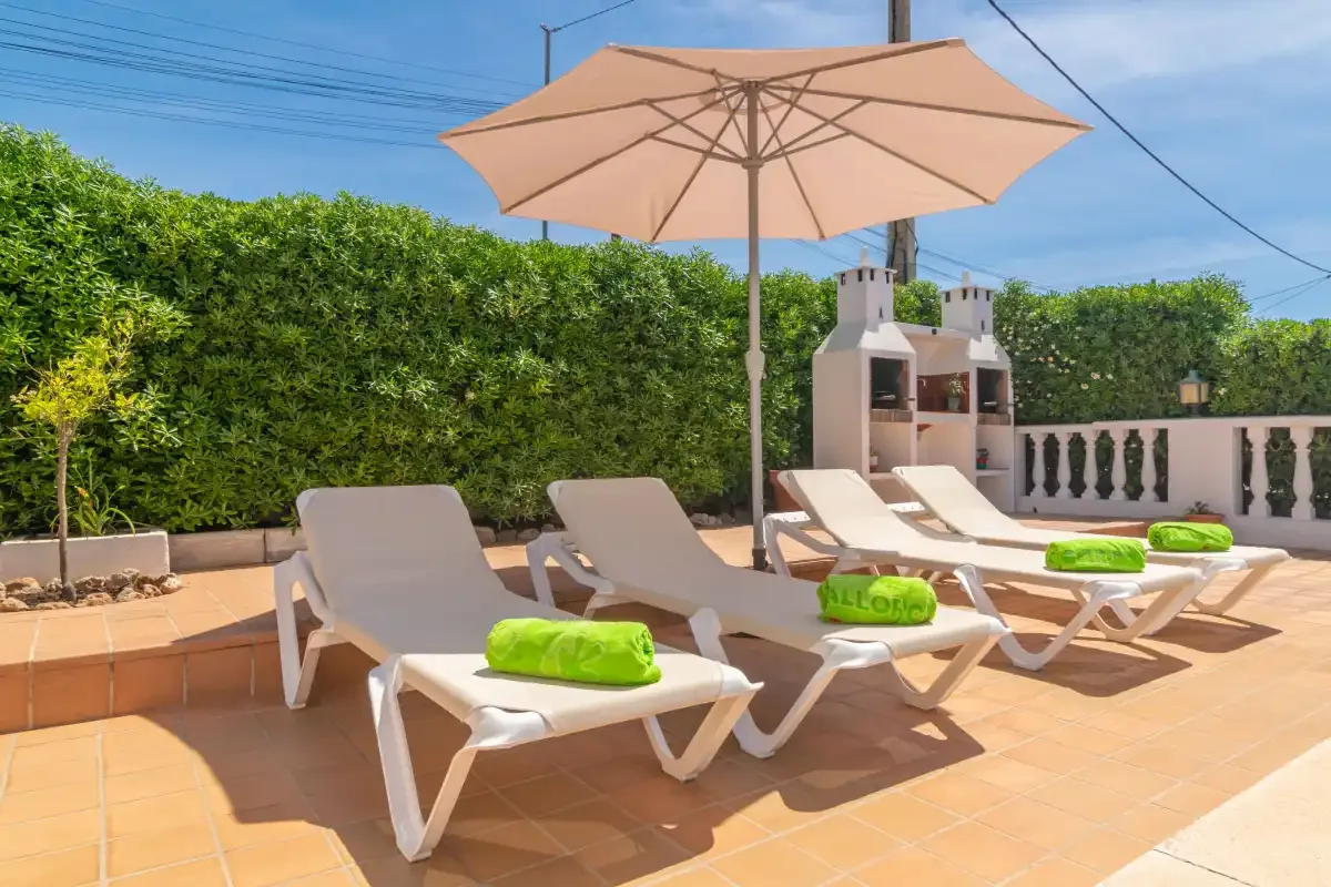 A sunny tiled terrace has lounge seating beneath a large umbrella.