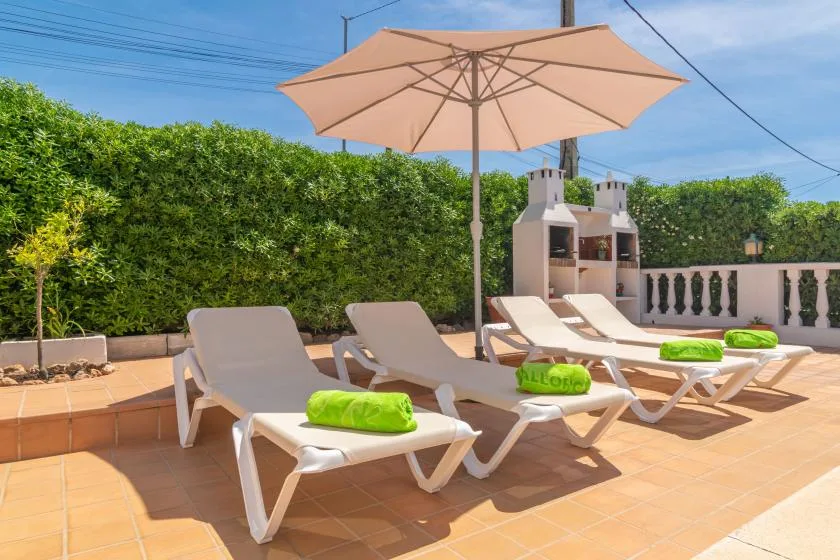 A sunny outdoor terrace has several loungers beneath a large umbrella.