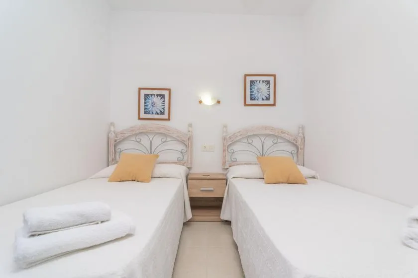 A bright bedroom with two single beds and framed pictures above them.