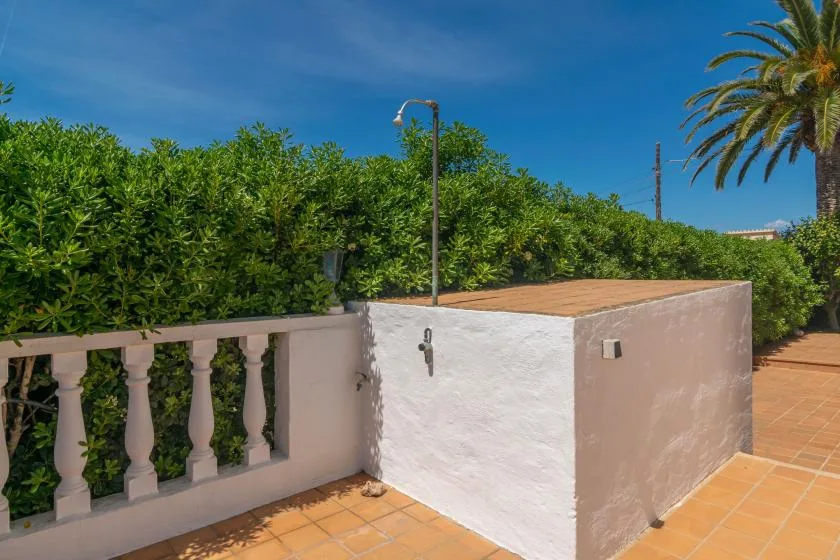 Outdoor terrace with tiled paving, a low wall, and dense green hedges.