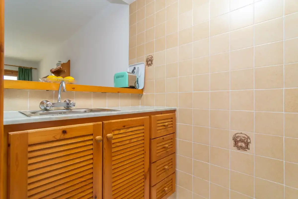 A bathroom vanity with a sink, wooden cabinets, and beige tiled walls.
