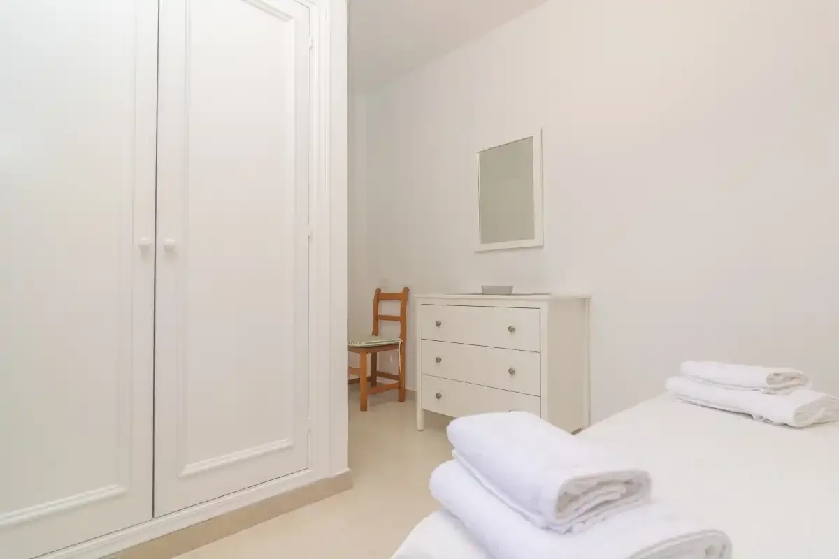 A bright bedroom with a bed, folded towels, and a white dresser.
