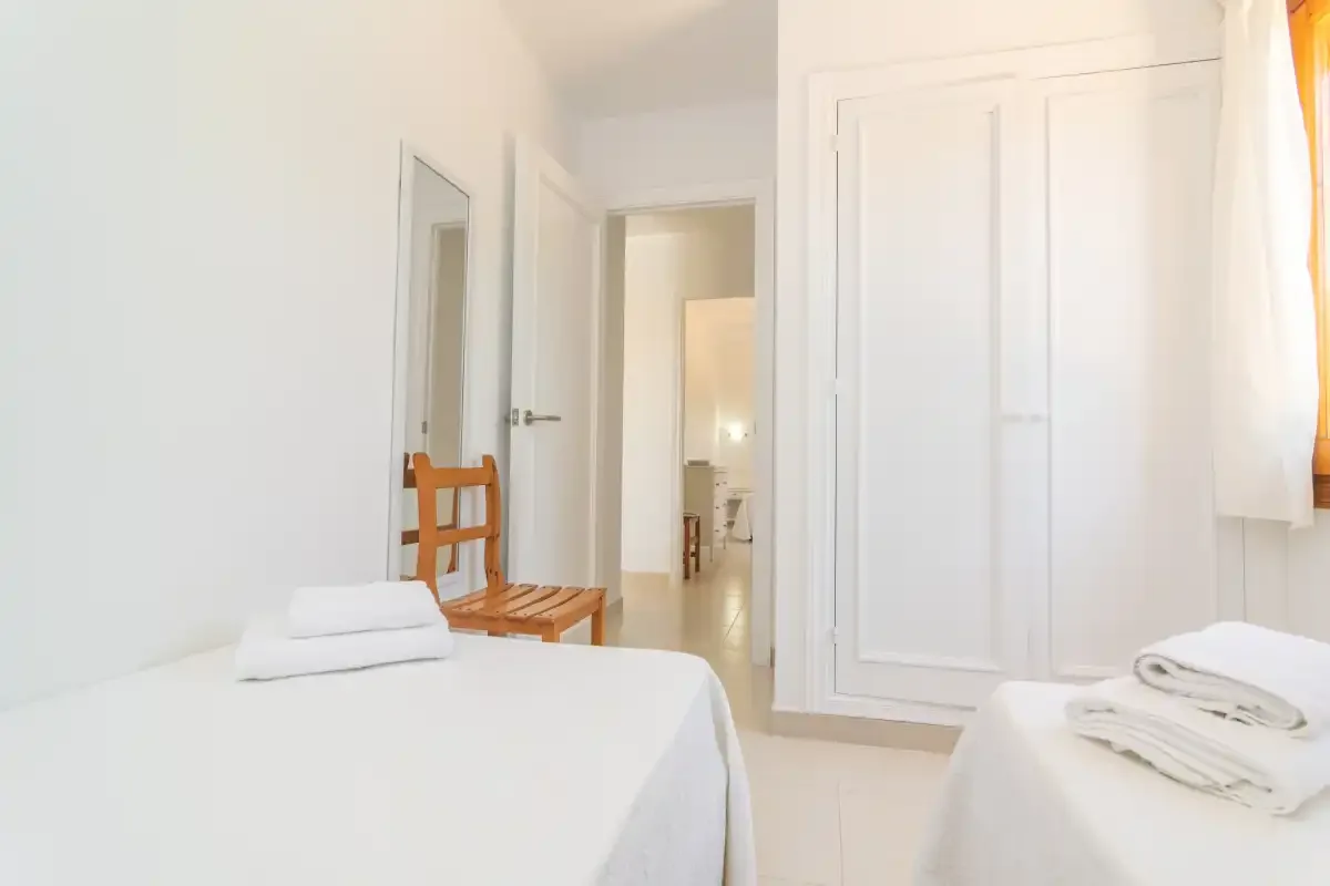 A bright bedroom with two beds and folded towels beside a white wardrobe.