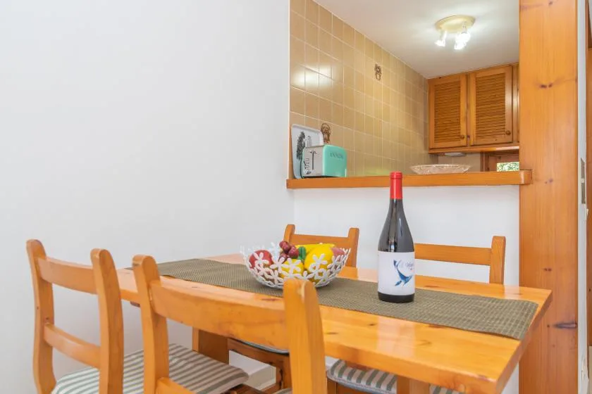A wooden dining table with chairs sits beside a tiled kitchen counter.