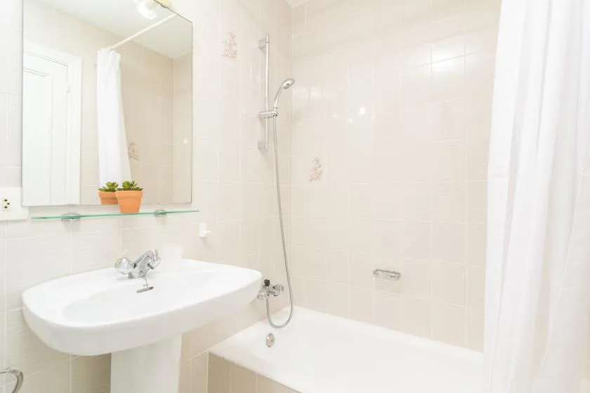 A bright tiled bathroom with a sink and a shower beside the bathtub.