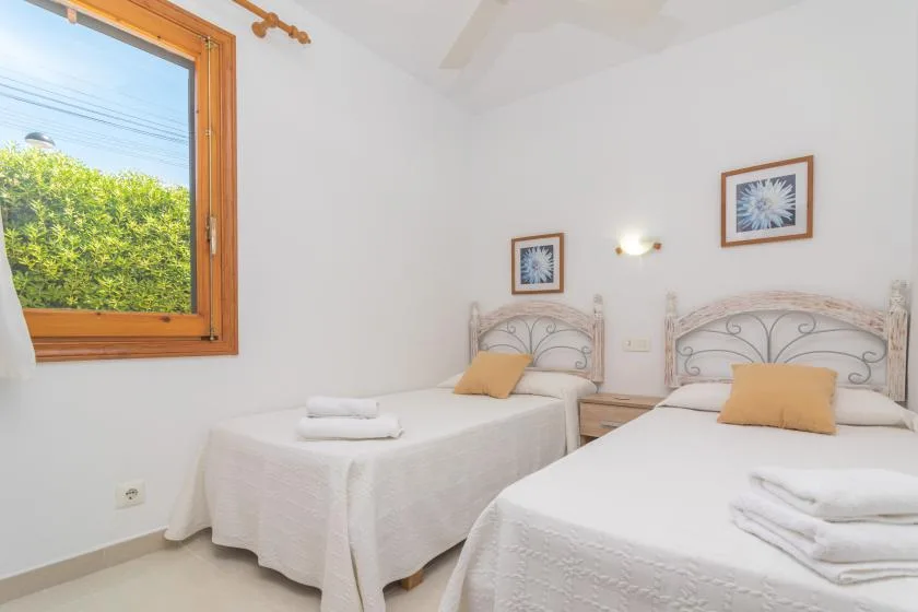 A bright bedroom with two beds and a large window overlooking greenery.