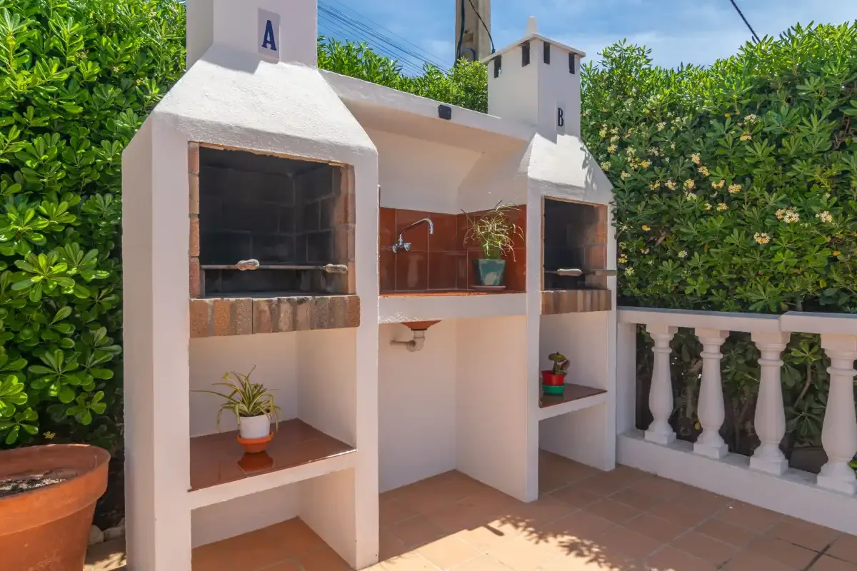 An outdoor cooking area with built-in grills and a sink, beside a balustrade.