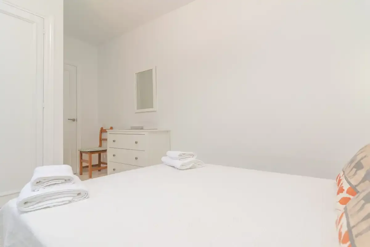 A bright bedroom with a bed, folded towels, and a dresser.