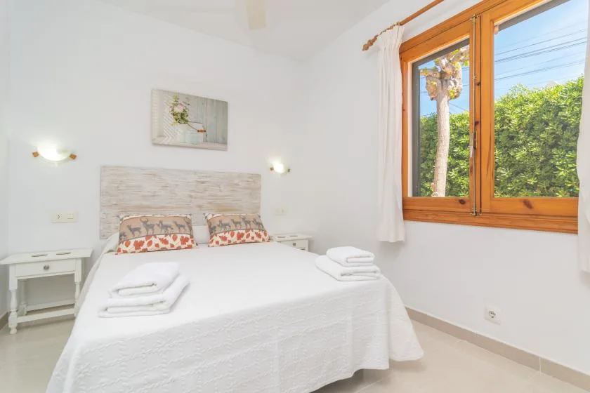 A bright bedroom with a neatly made bed and a large wooden-framed window.