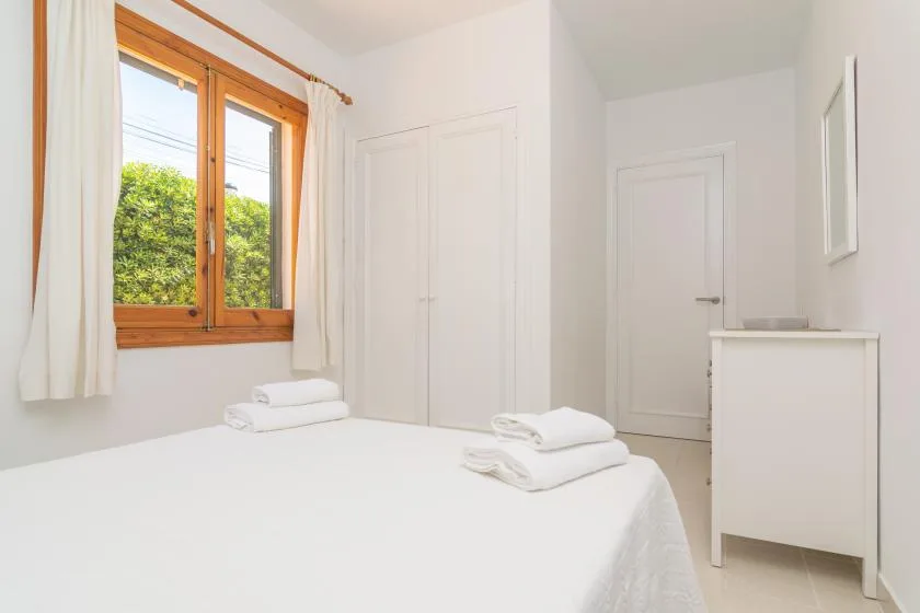 A bright bedroom with a bed beside a wood-framed window.