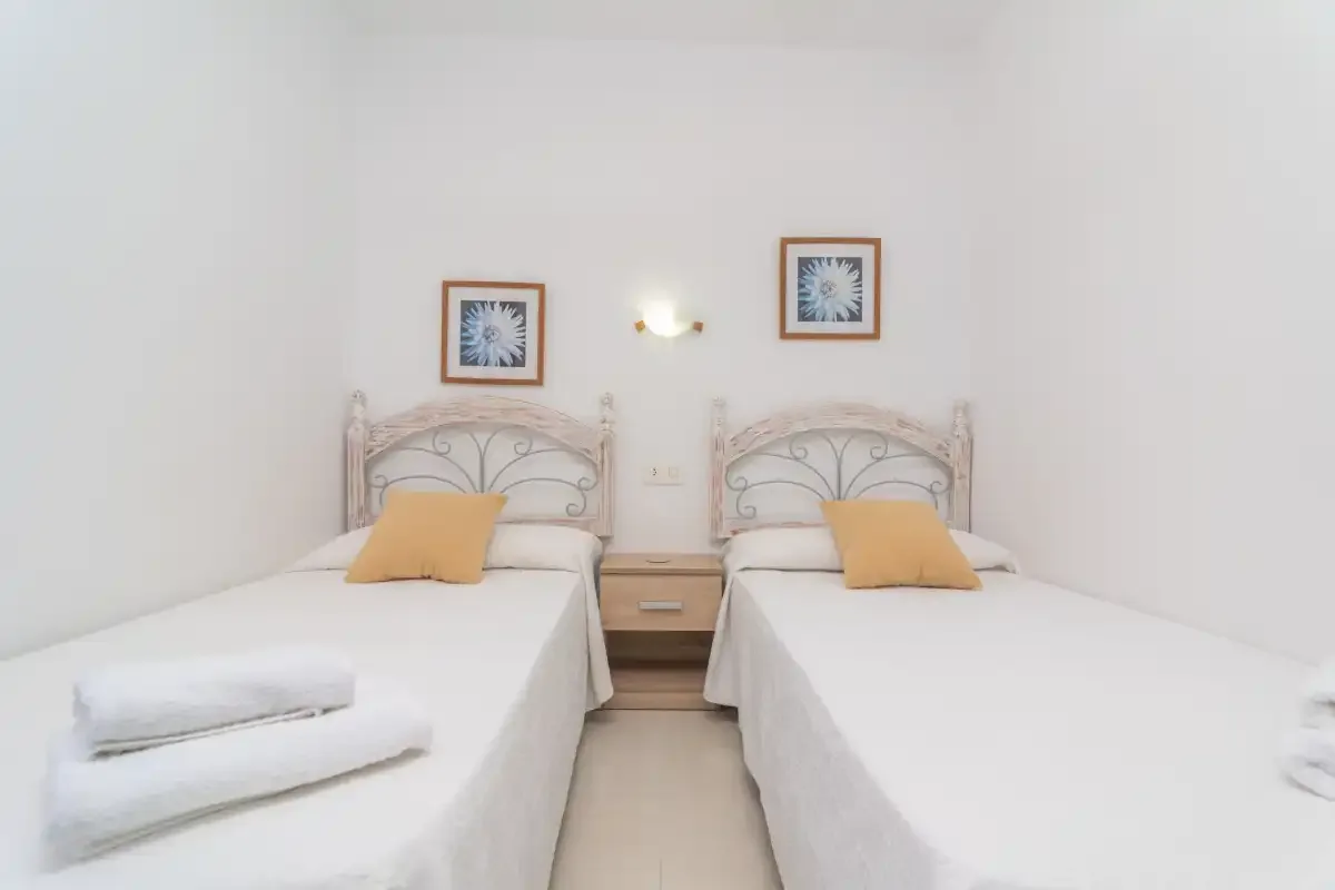 A twin bedroom with two beds, framed pictures, and a small bedside table.