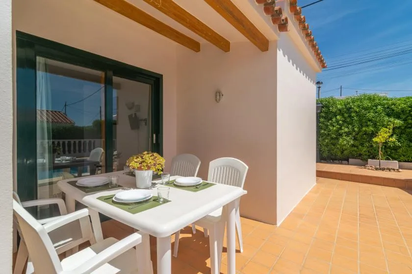 An outdoor dining area with a white table and chairs beside a glass door.