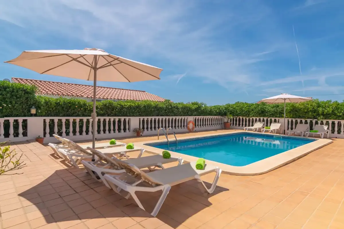 A sunny outdoor pool area has lounge seating and umbrellas on a tiled terrace.