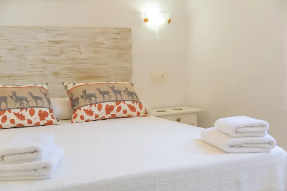A bedroom with a white bed, patterned pillows, and folded towels.