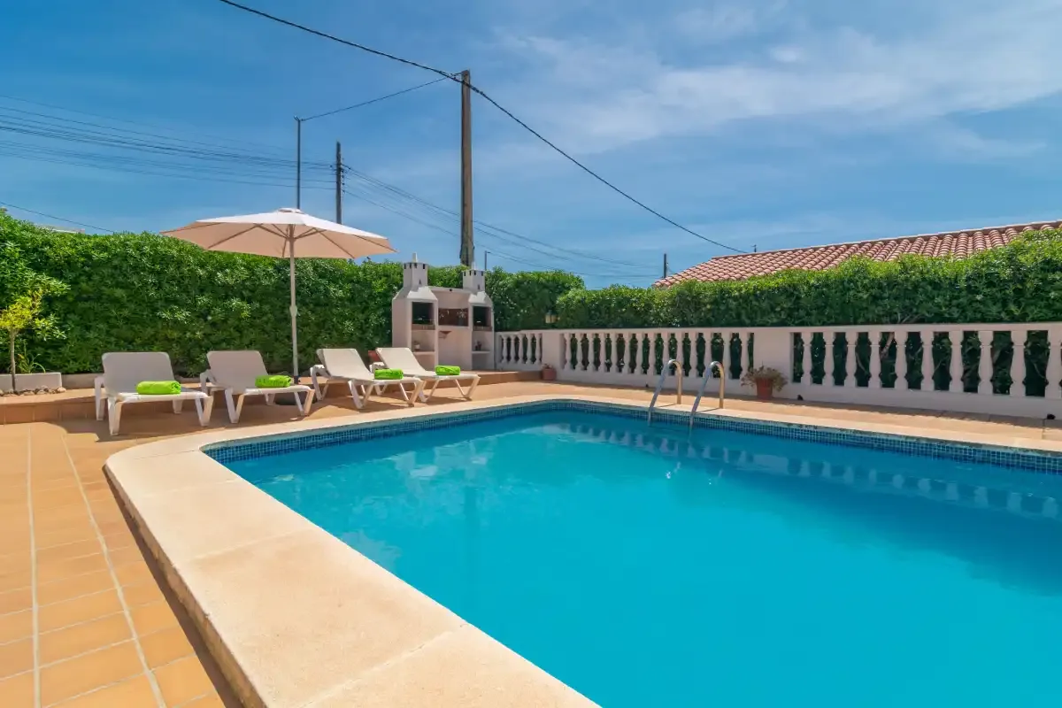 A swimming pool fills a sunlit outdoor terrace with lounge seating nearby.