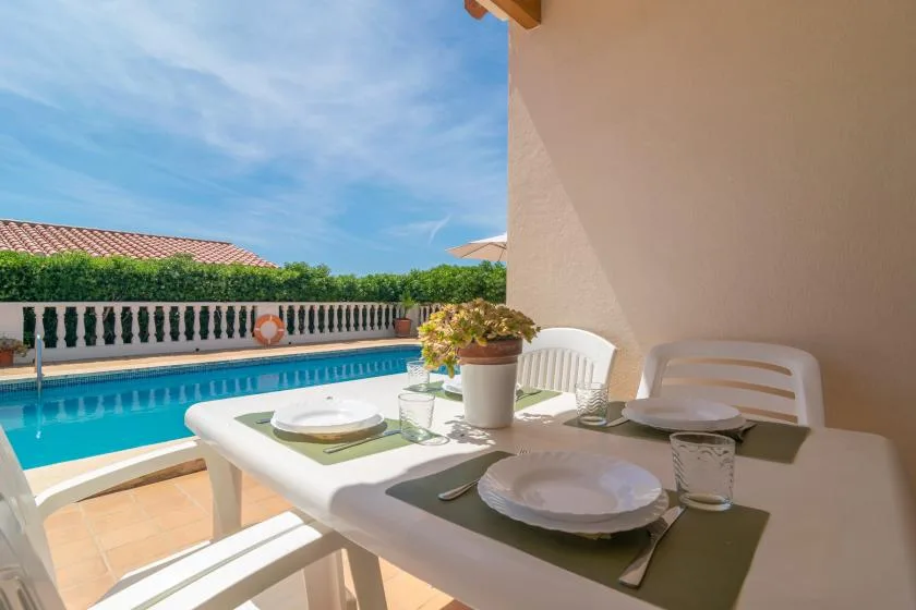 A patio dining table overlooks a swimming pool and garden.