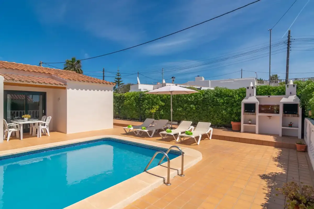 A sunny patio with a swimming pool, lounge seating, and a built-in barbecue.