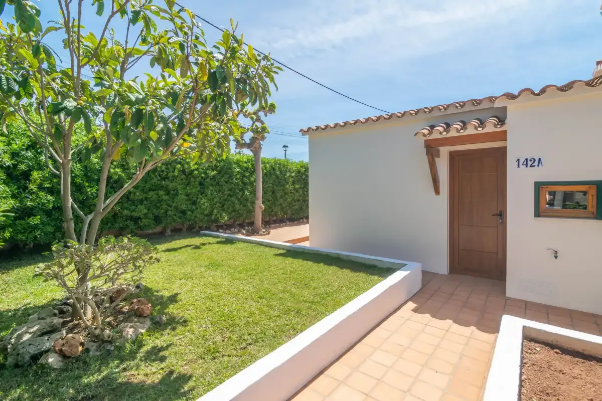 A garden path leads to a white stucco building with a wooden door.