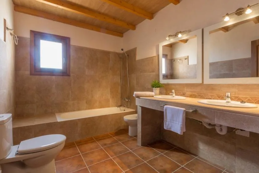 Un baño alicatado con bañera, inodoro y un largo lavabo bajo dos espejos.