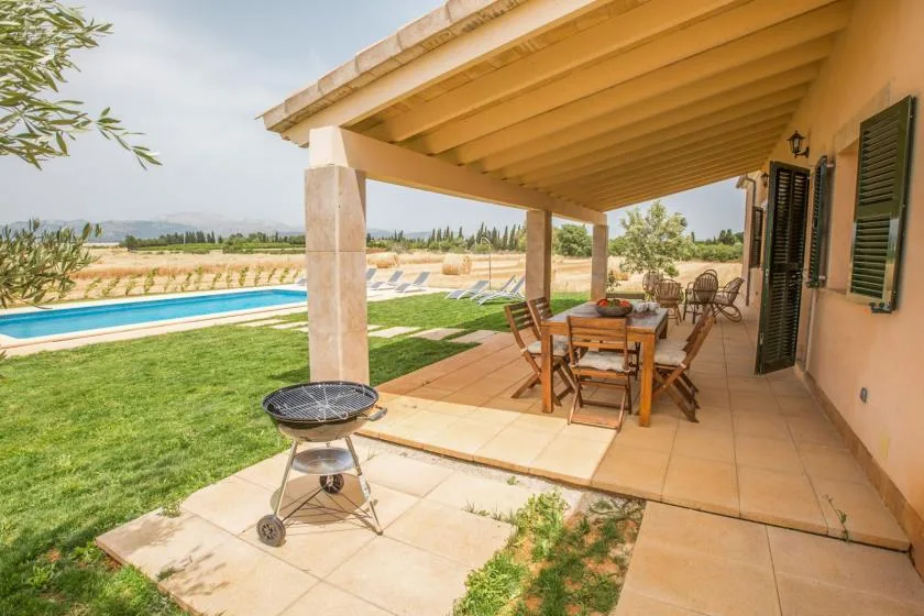 Un patio cubierto con una mesa de comedor exterior da a un jardín y una piscina.