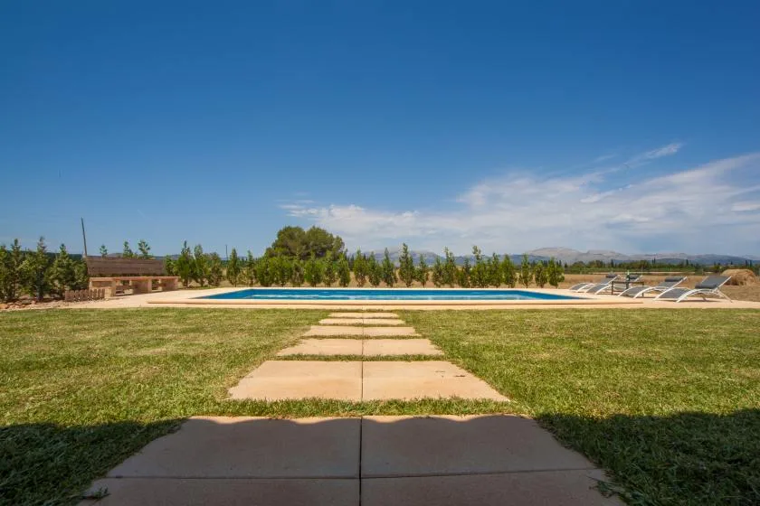 Una piscina al aire libre se encuentra tras un sendero pavimentado en un jardín con césped.